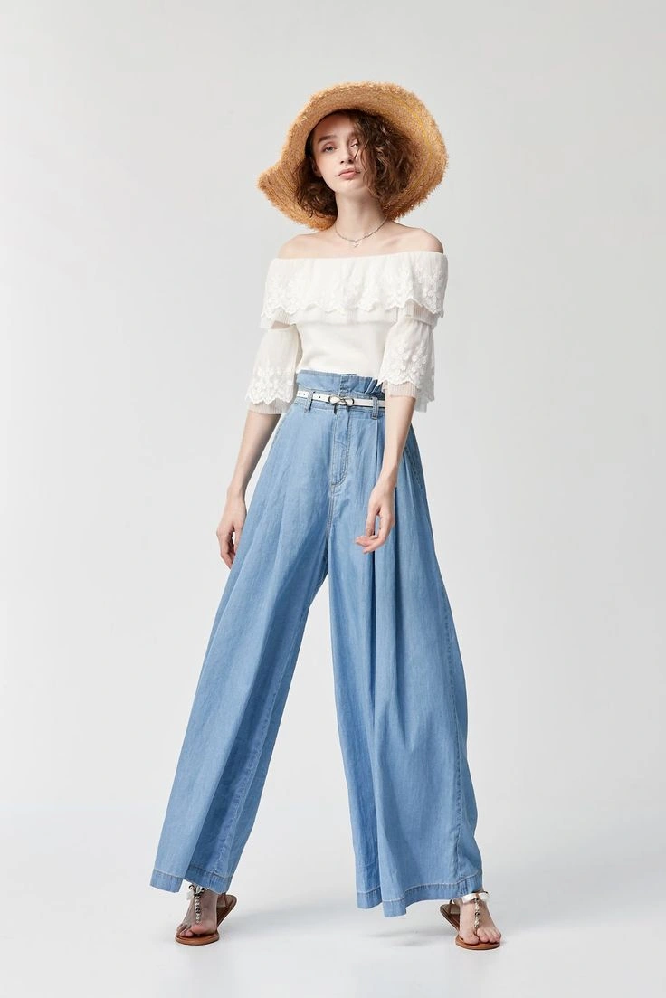 챙이 넓은 밀짚모자와 오프숄더 흰색 레이스 블라우스, 하이웨이스트 연청색 와이드 팬츠를 입고 포즈를 취하는 여성